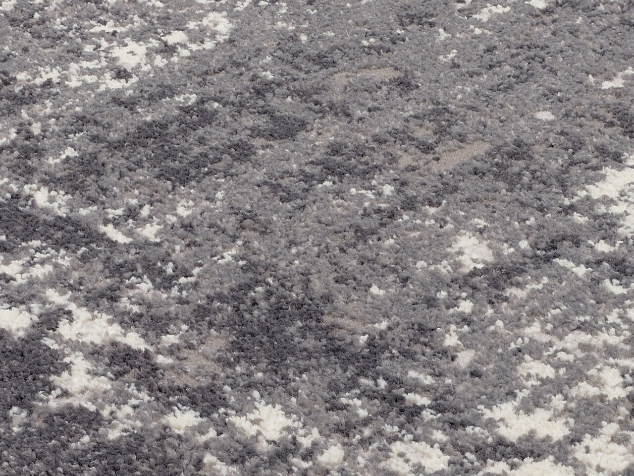 Nahaufnahme eines Designer-Teppichs mit grauem und weißem Muster, aus seitlicher Perspektive fotografiert.