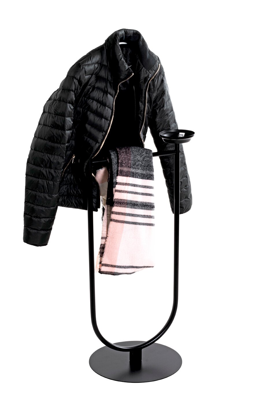 Schwarzer, freistehender Garderobenständer aus Metall mit rundem Standfuß und Ablageschale, von vorn leicht seitlich fotografiert, mit aufgehängter schwarzer Steppjacke und rosa-grau kariertem Schal vor weißem Hintergrund