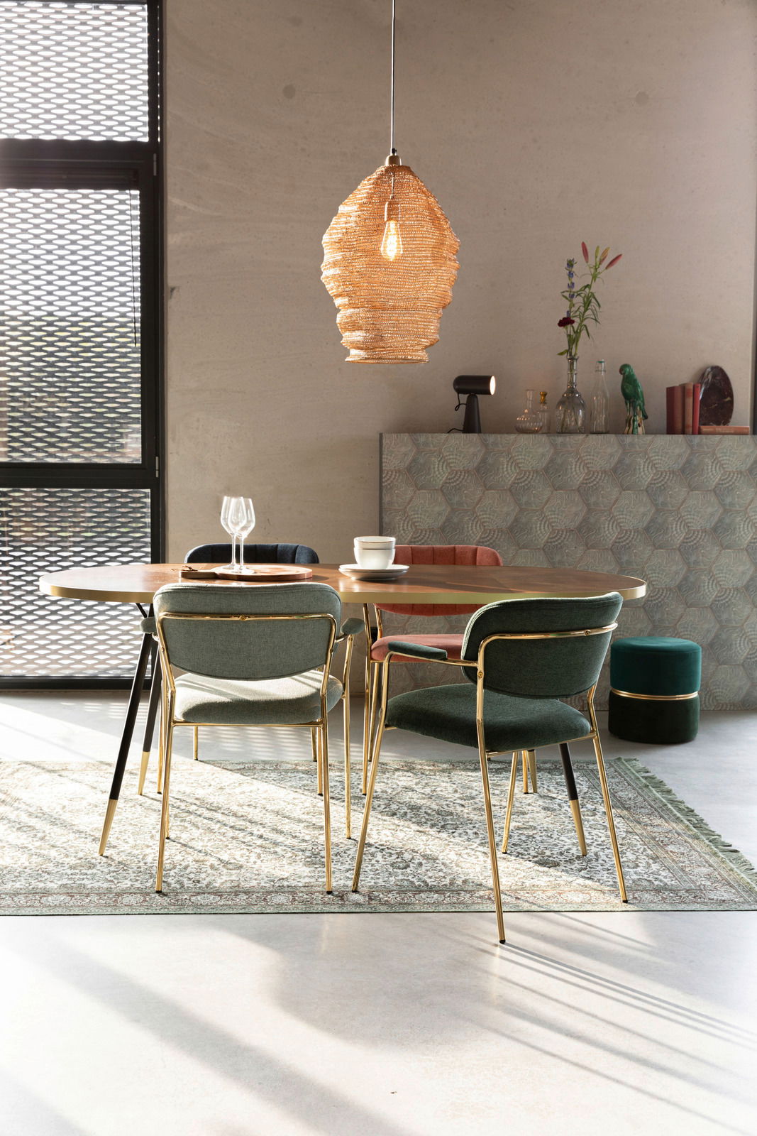 Esszimmer mit einem runden Tisch und mehreren Armlehnenstühlen in verschiedenen Farben, von hinten betrachtet. Im Hintergrund eine moderne Hängelampe und Dekorationen.