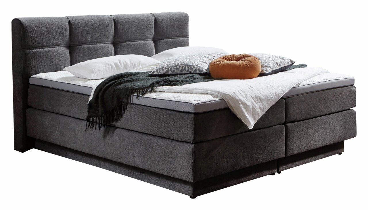 Boxspringbett in dunklem Stoffbezug mit hohem, gepolstertem Kopfteil, seitliche Perspektive