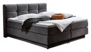 Boxspringbett in dunklem Stoffbezug mit hohem, gepolstertem Kopfteil, seitliche Perspektive