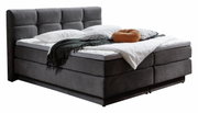 Boxspringbed met een donkere stoffen bekleding en een hoog, gestoffeerd hoofdeinde, gezien vanaf de zijkant