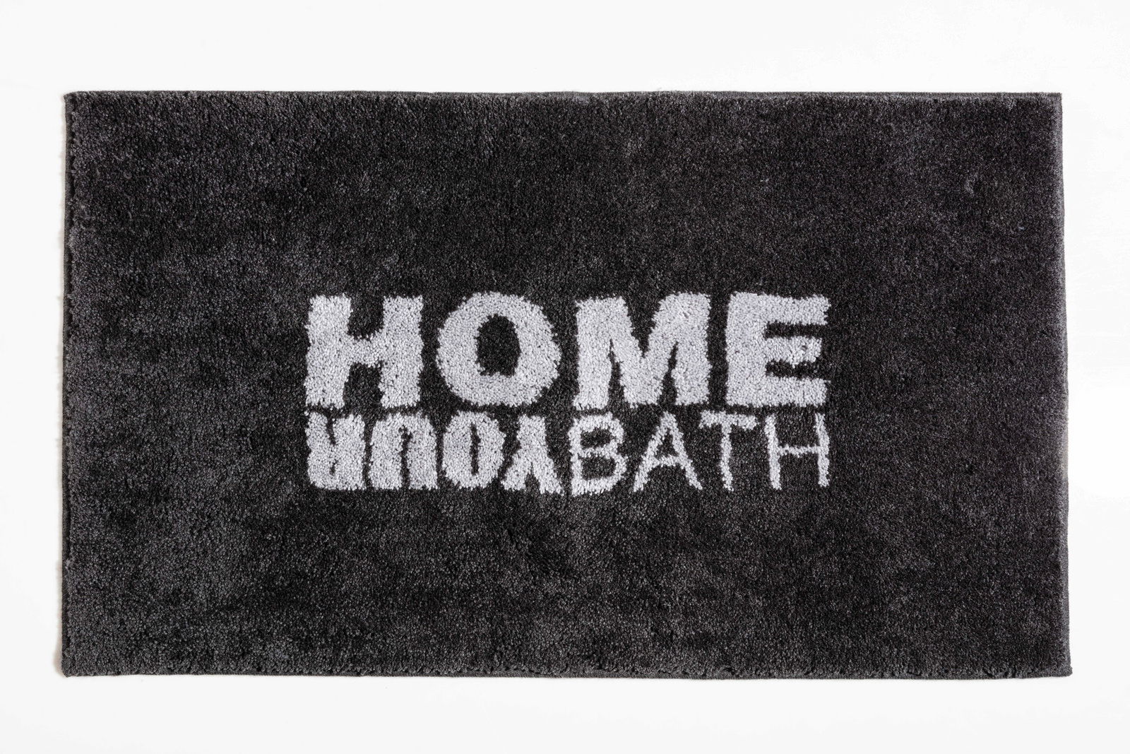 Schwarzer Badteppich mit der Aufschrift 'HOME YOUR BATH' in weißer Schrift, von oben betrachtet.