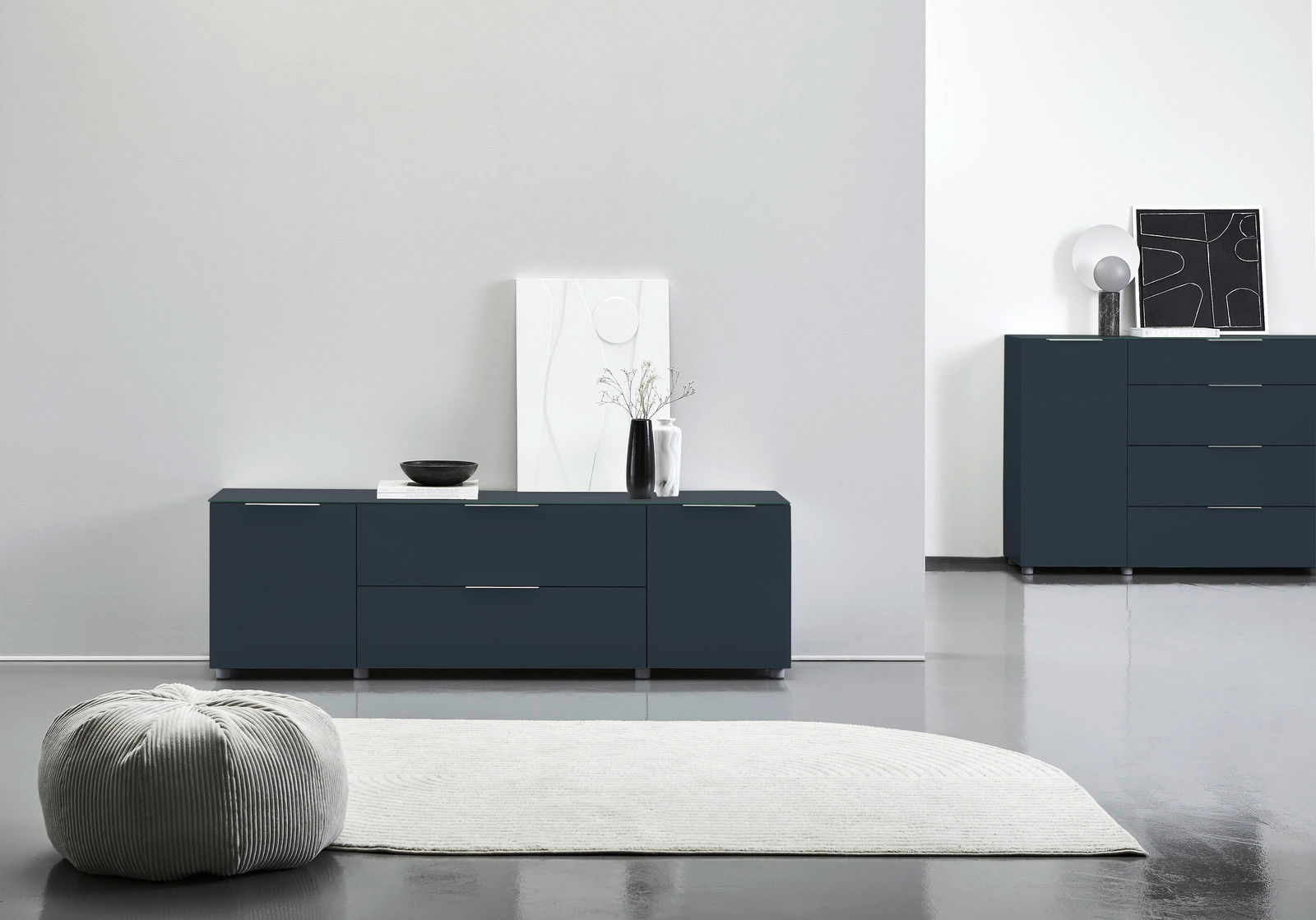 Voleo Tv-kast MALIN Modernes TV-Lowboard in dunklem Blau mit klaren Linien, frontal fotografiert. Dekoriert mit einer Vase und Kunstobjekten, steht es auf einem glänzenden Boden neben einem Teppich.