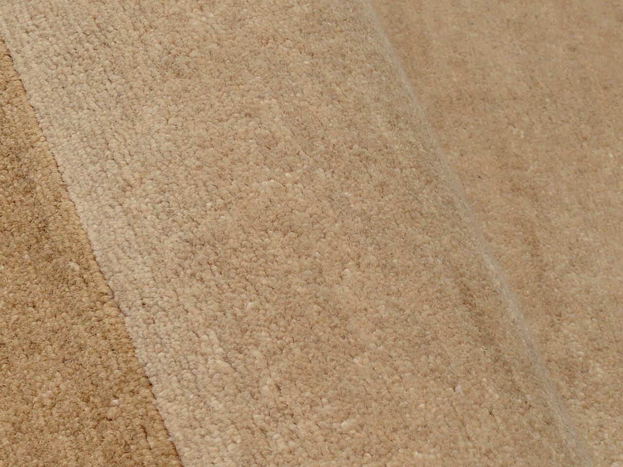 Nahaufnahme eines beigen Wollteppichs mit weicher Textur, schräg von der Seite fotografiert.