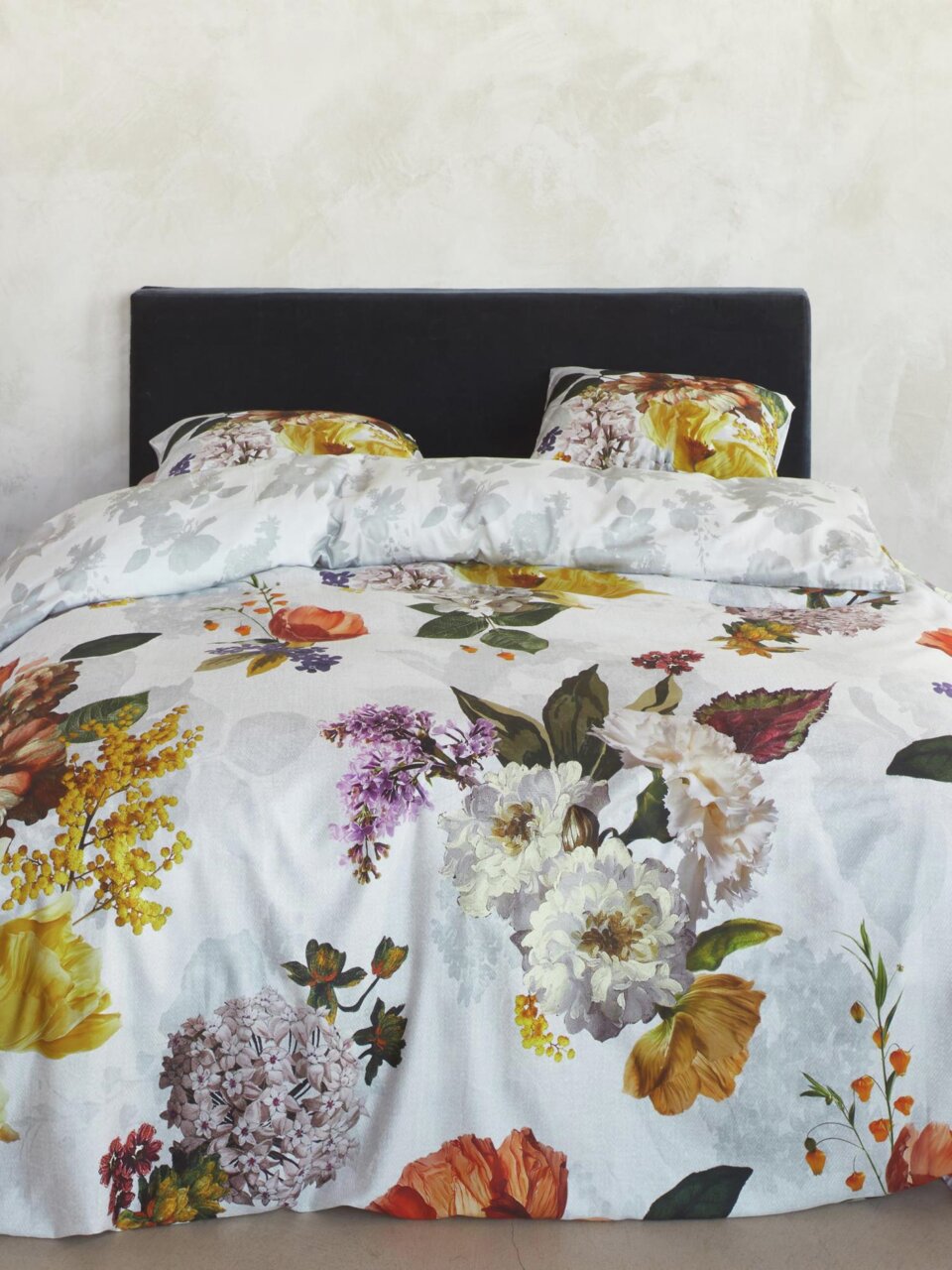 Bettwäsche-Set mit floralem Muster in verschiedenen Farben, bestehend aus einem Bettbezug und zwei Kissenbezügen, auf einem Bett mit schwarzem Kopfteil, frontal fotografiert.