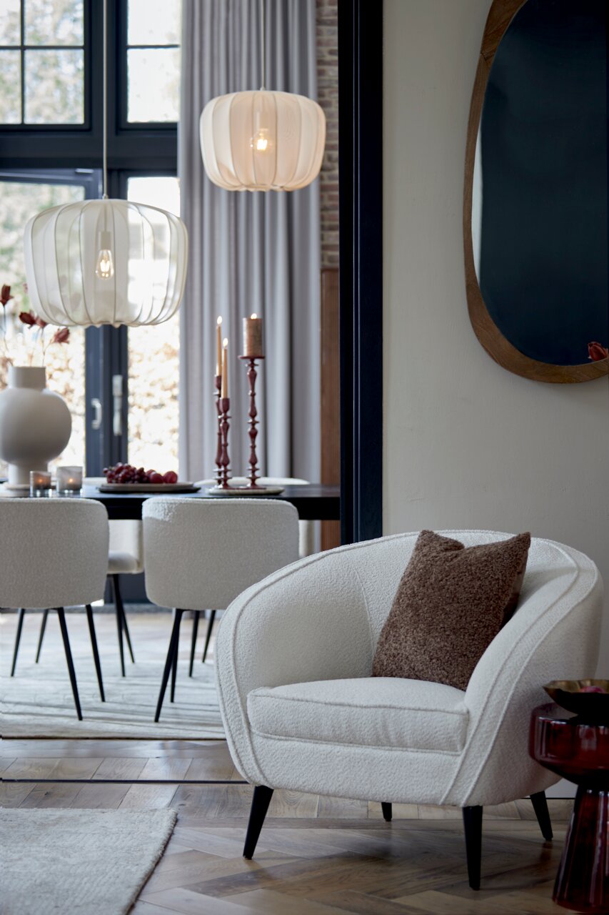 Braunes Kissen LINA 45x45 cm auf einem cremefarbenen Sessel in einem stilvoll eingerichteten Wohnzimmer, seitliche Perspektive.