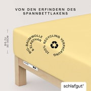 Nahaufnahme eines gelben Spannbettlakens auf einer Matratze, hergestellt aus Bio-Baumwolle und Elasthan, mit Recycling-Verpackung. Perspektive von der Seite.