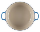 Blick von oben auf einen runden blauen Bräter mit zwei Griffen, Innenansicht in Beige.