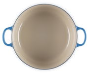 Blick von oben auf einen runden blauen Bräter mit zwei Griffen, Innenansicht in Beige.