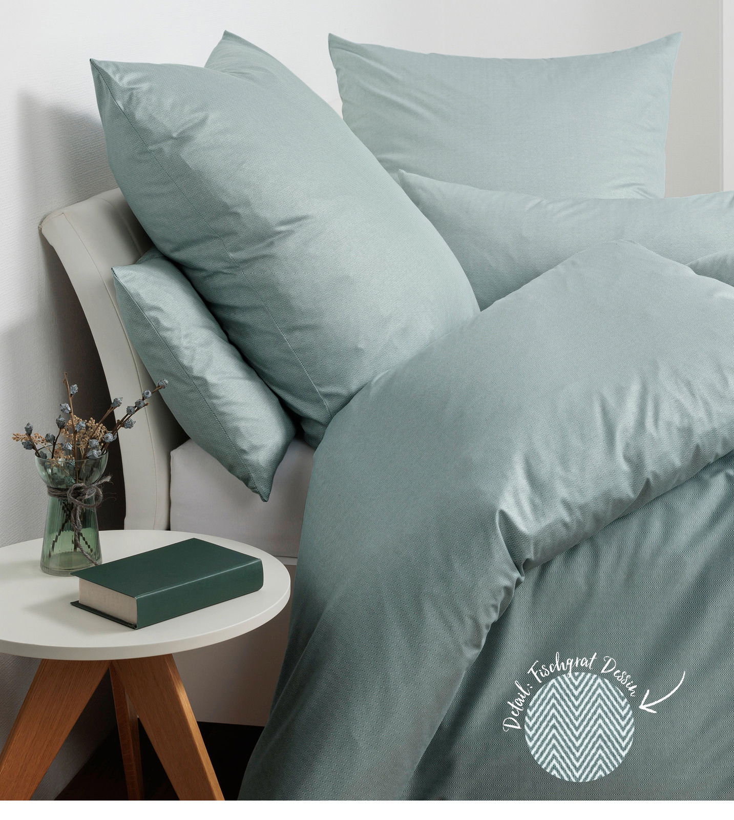 Janine Beddengoed JERSEY-CLASSIC Bettwäsche-Set in sanftem Grün auf einem Bett, bestehend aus Kissen und Decke, mit Fischgratmuster. Perspektive von der Seite mit einem Nachttisch im Vordergrund.