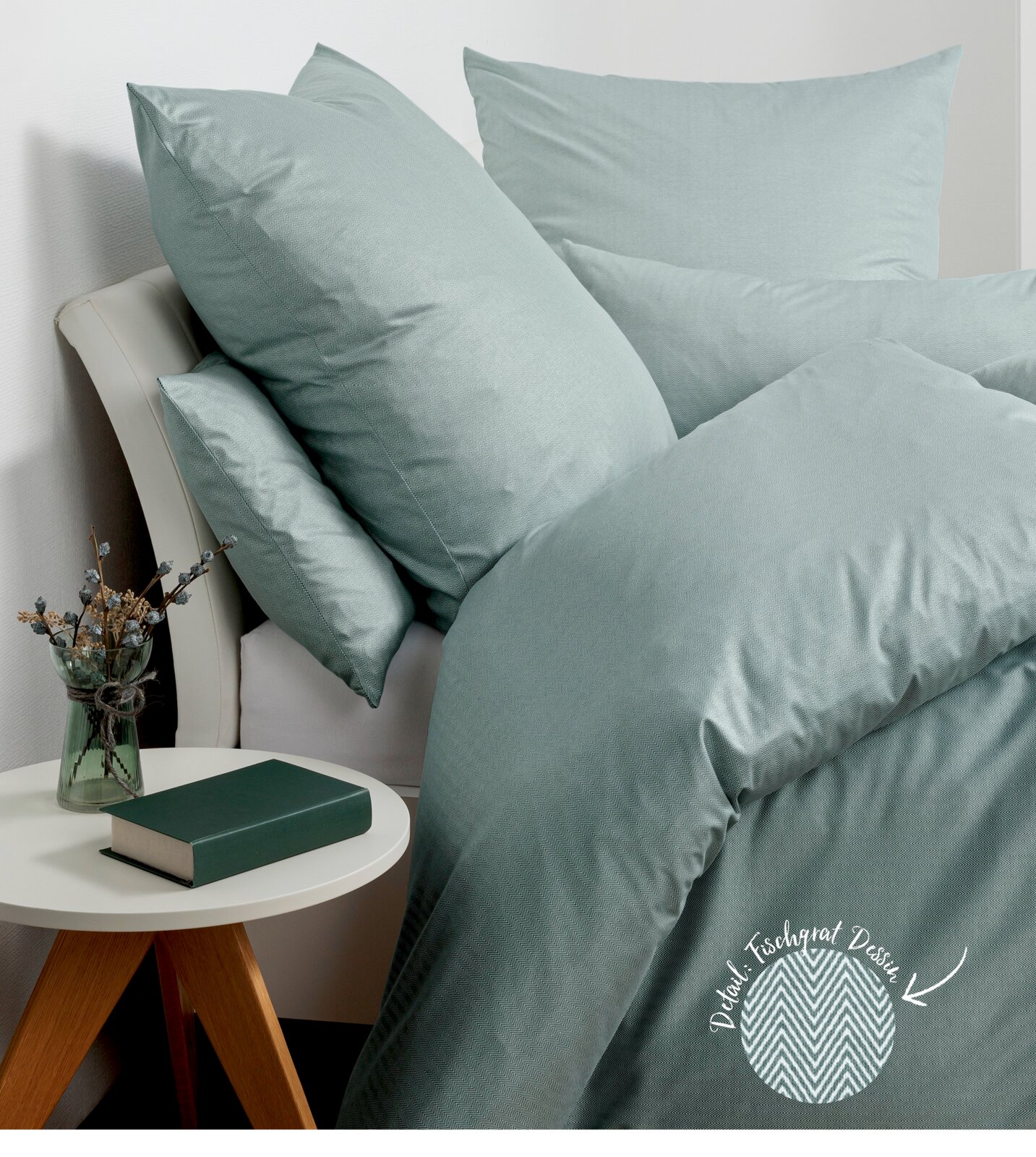 Bettwäsche-Set in sanftem Grün auf einem Bett, bestehend aus Kissen und Decke, mit Fischgratmuster. Perspektive von der Seite mit einem Nachttisch im Vordergrund.