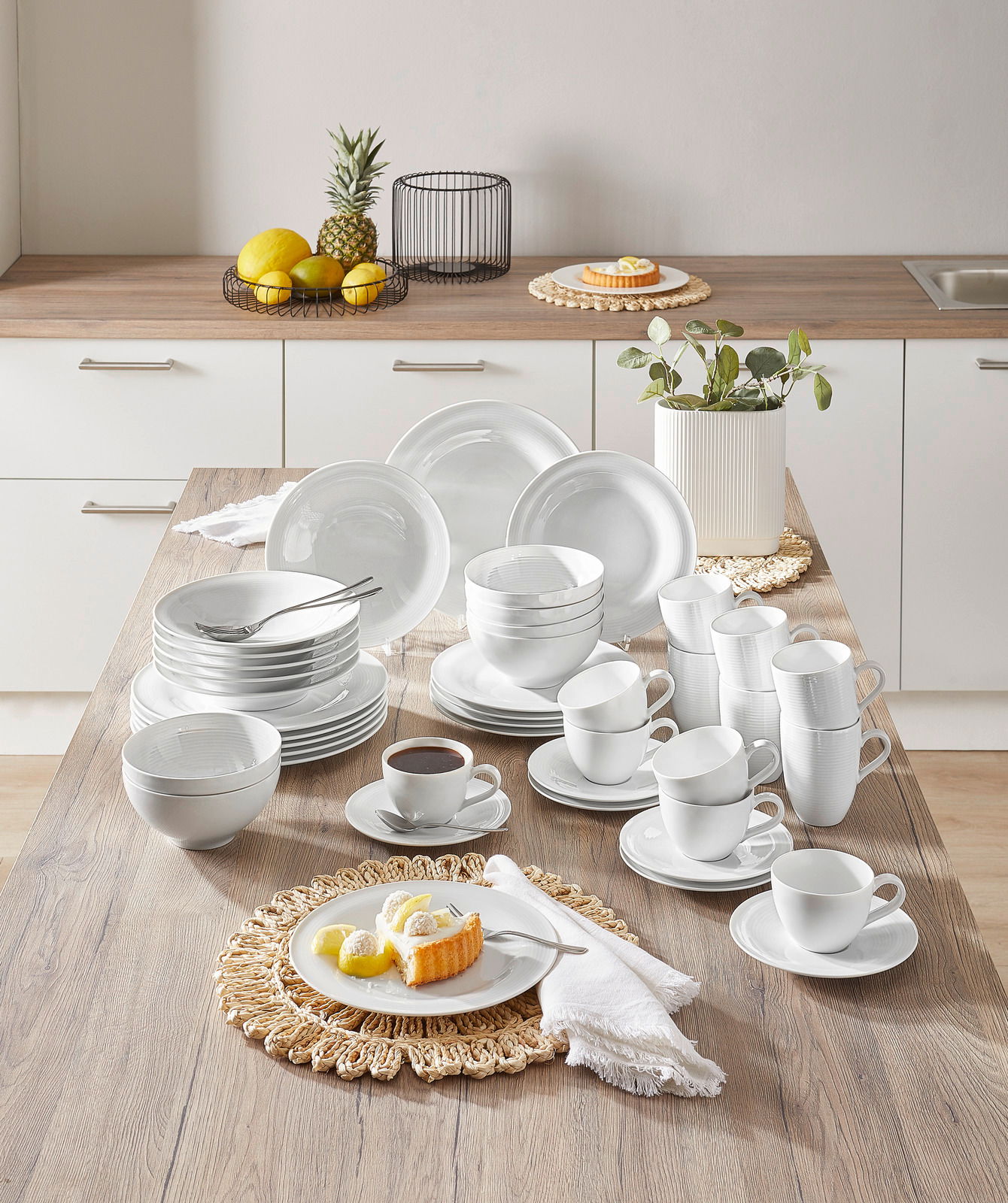 Kombiservice Beat 42-tlg. in einer modernen Küche, von oben fotografiert. Das Set umfasst Teller, Schalen und Tassen in elegantem Weiß, arrangiert auf einem Holztisch.