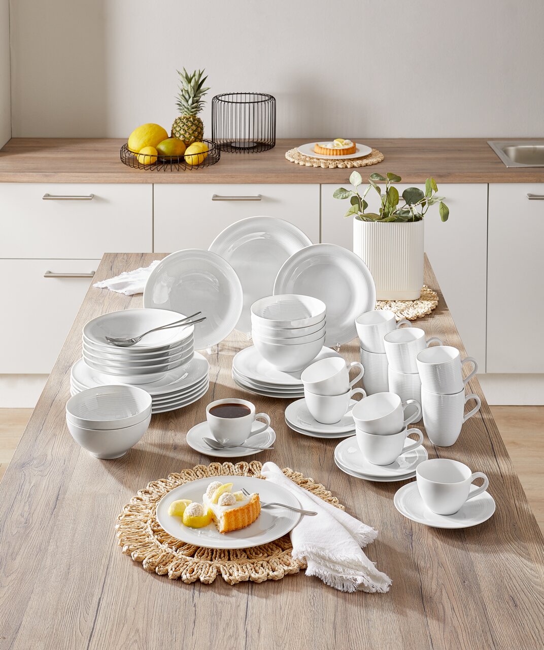 Kombiservice Beat 42-tlg. in einer modernen Küche, von oben fotografiert. Das Set umfasst Teller, Schalen und Tassen in elegantem Weiß, arrangiert auf einem Holztisch.