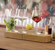 Drie elegante gin-tonicglazen met rietjes op een houten plank, omringd door munt, citroen en barbenodigdheden, gefotografeerd vanuit een zijaanzicht.