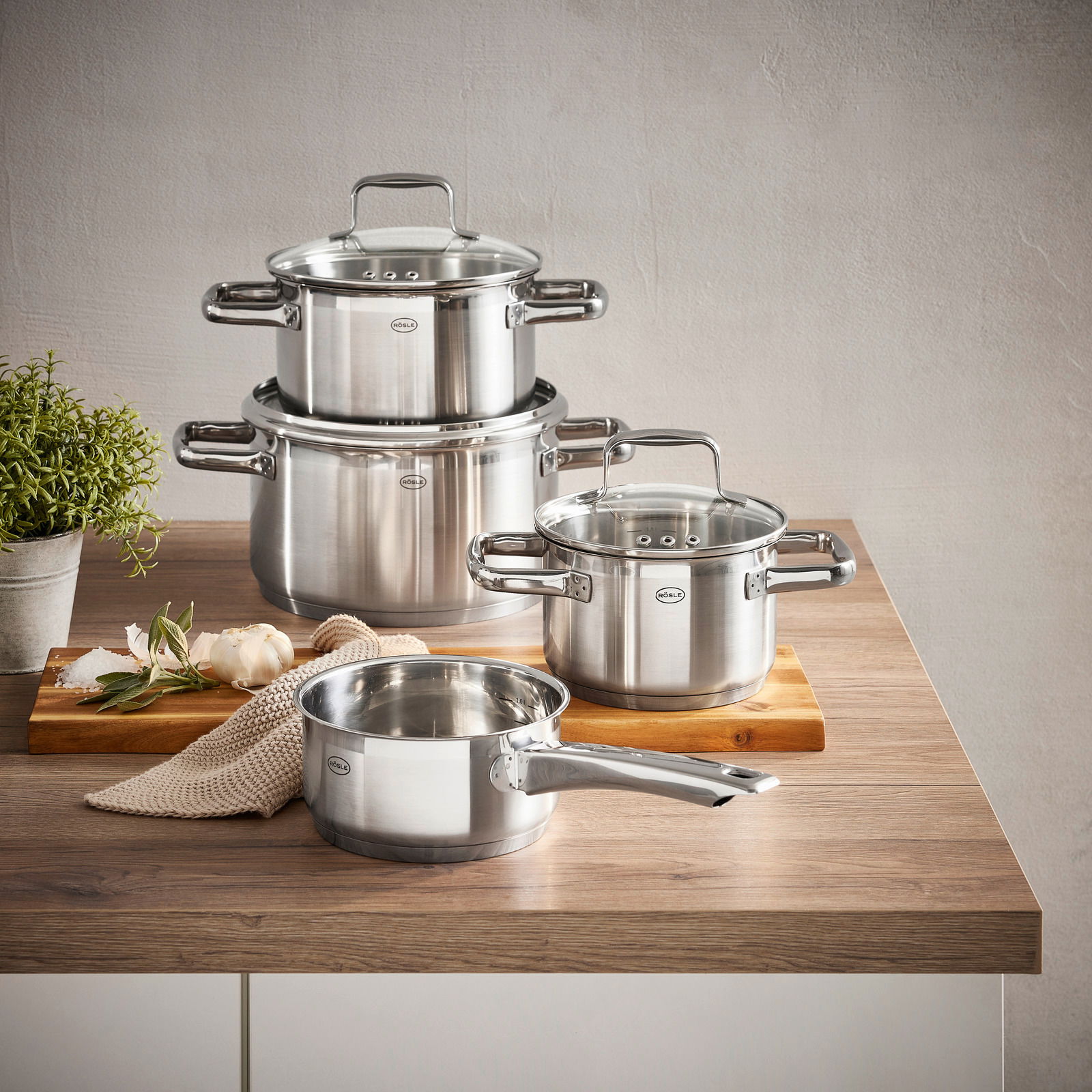 Topfset Charm 4-tlg. aus Edelstahl, bestehend aus drei Töpfen und einer Stielkasserolle, auf einem Holztisch von schräg oben fotografiert.