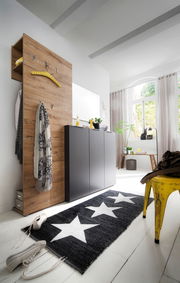 Moderner Flur mit einem Aufsatz-Garderobenpaneel aus Holzoptik, an dem Jacken und Schals hängen. Daneben ein eleganter, dunkler Schuhschrank. Perspektive von schräg vorne.