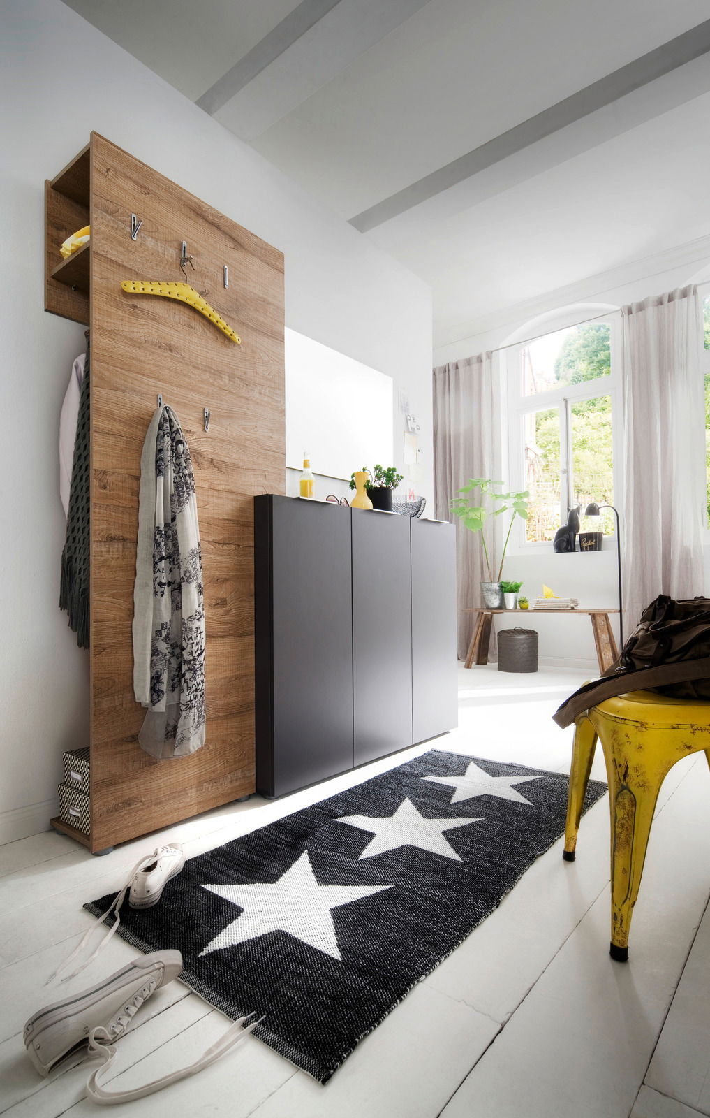 Moderner Flur mit einem Aufsatz-Garderobenpaneel aus Holzoptik, an dem Jacken und Schals hängen. Daneben ein eleganter, dunkler Schuhschrank. Perspektive von schräg vorne.