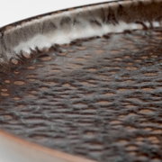 Makroaufnahme aus schräger Seitenperspektive einer rustikalen Keramikschale mit dunkelbrauner, gesprenkelter Glasur und leicht erhöhtem Rand