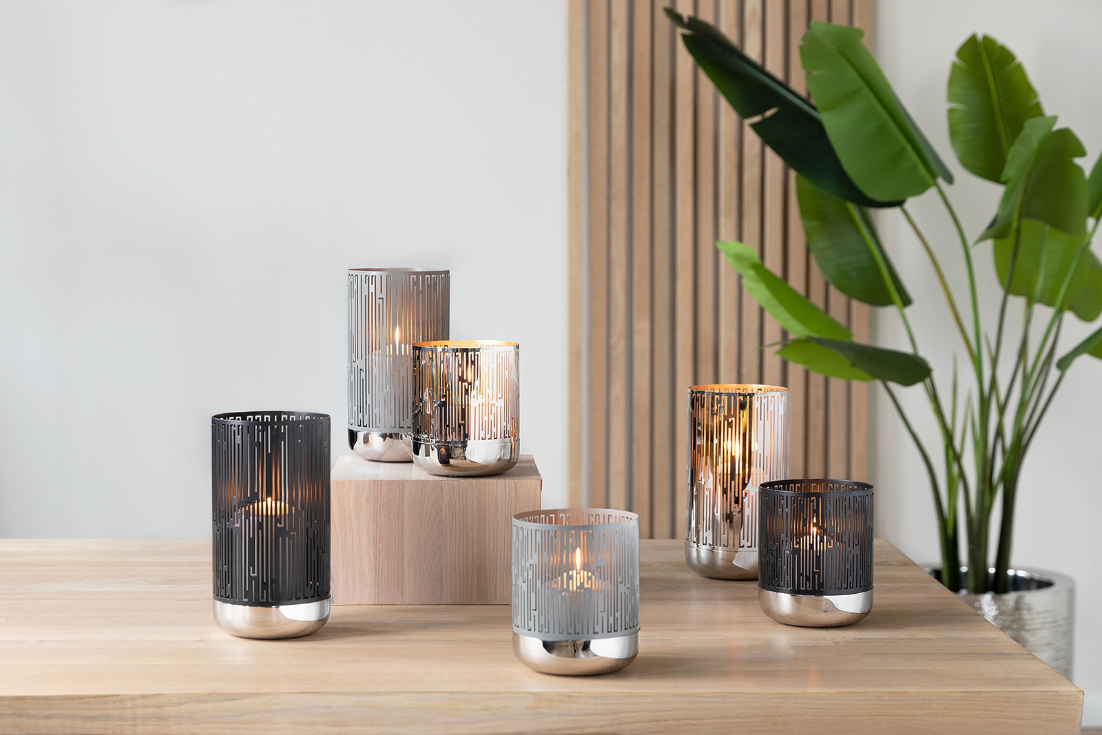 Mehrere Fink Windlichter BRIANO in verschiedenen Farben auf einem Tisch, mit einer modernen, eleganten Optik. Perspektive von vorne.