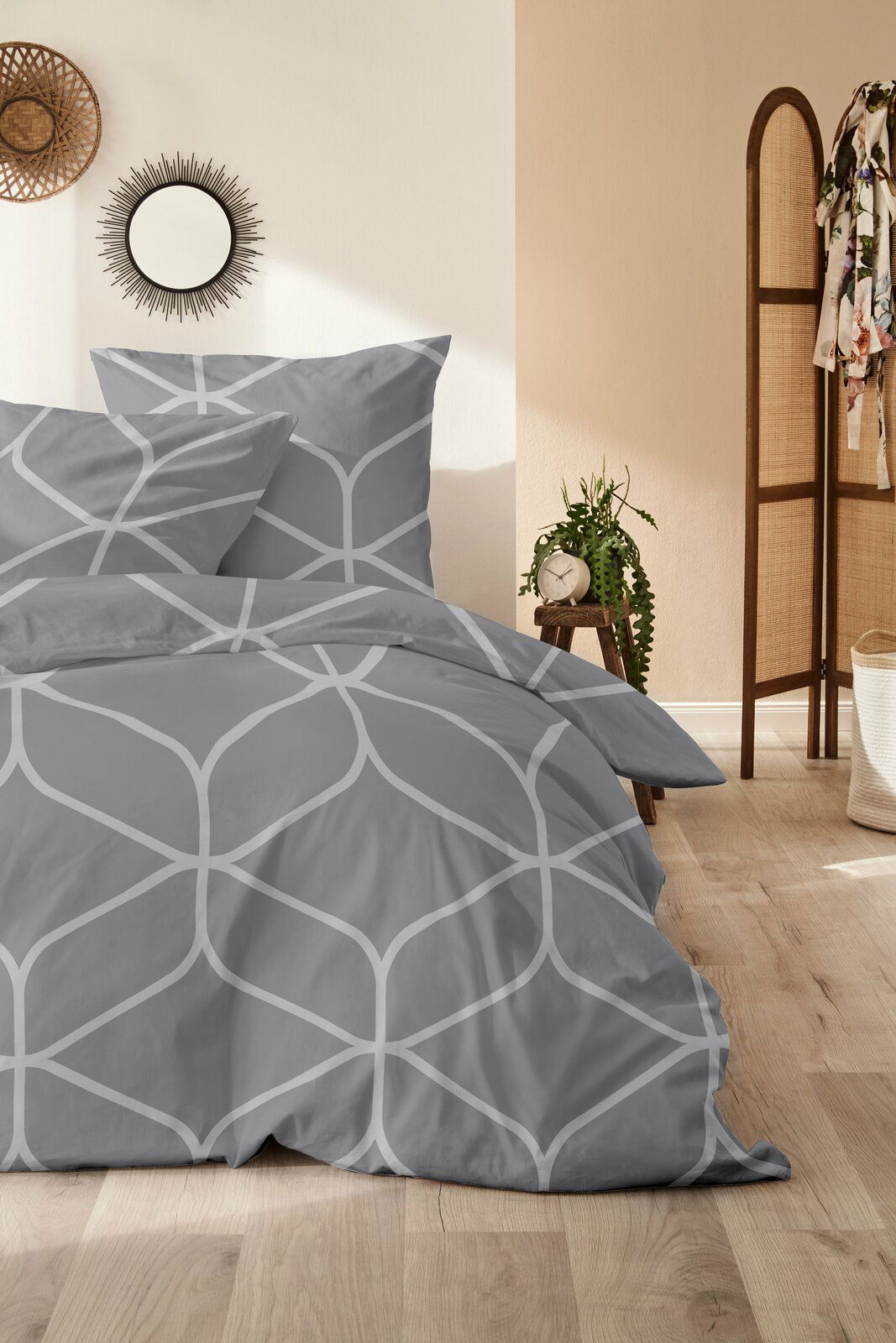 Graue Bettwäsche mit geometrischem Muster in einem stilvoll eingerichteten Schlafzimmer, seitliche Perspektive.