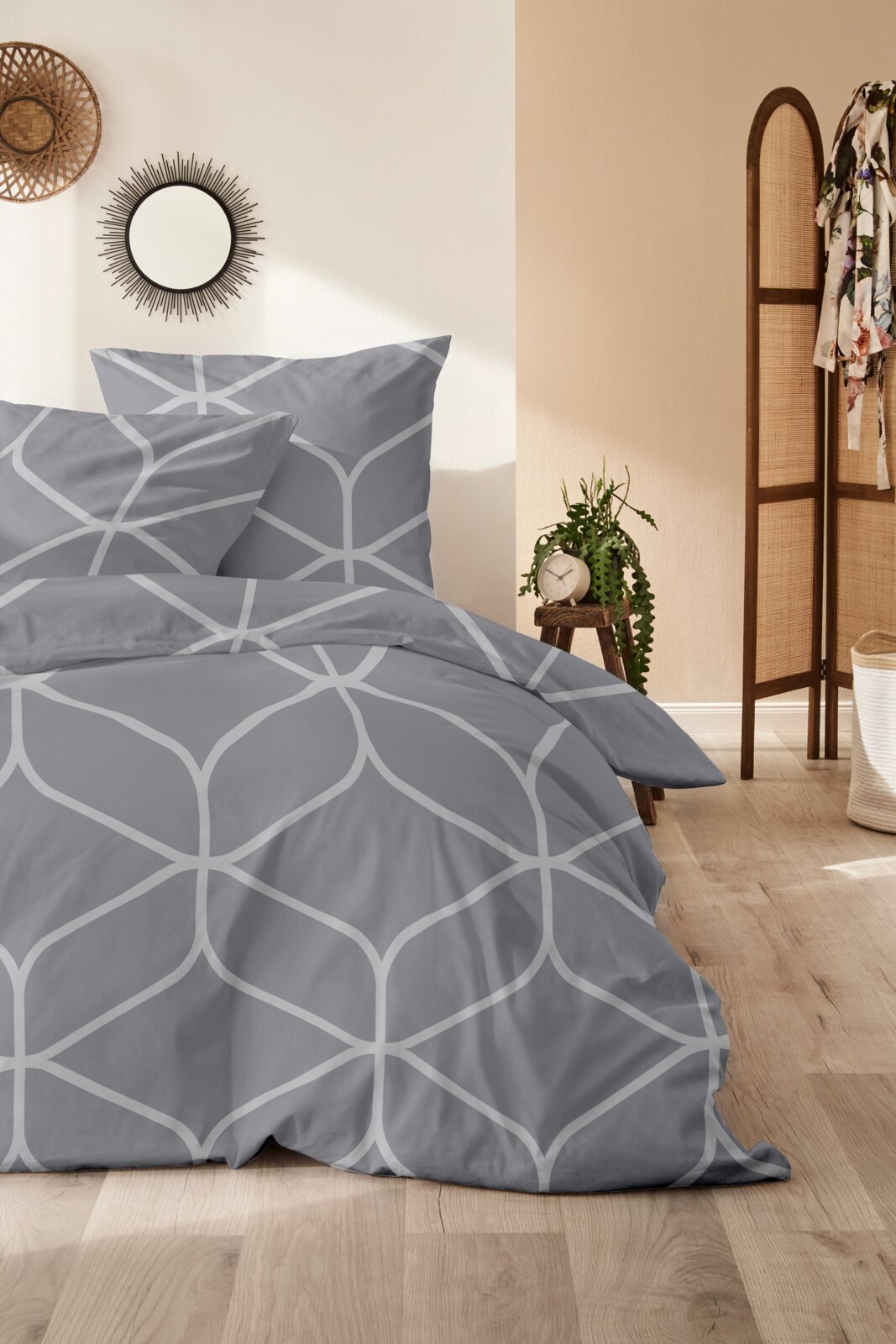 Graue Bettwäsche mit geometrischem Muster in einem stilvoll eingerichteten Schlafzimmer, seitliche Perspektive.