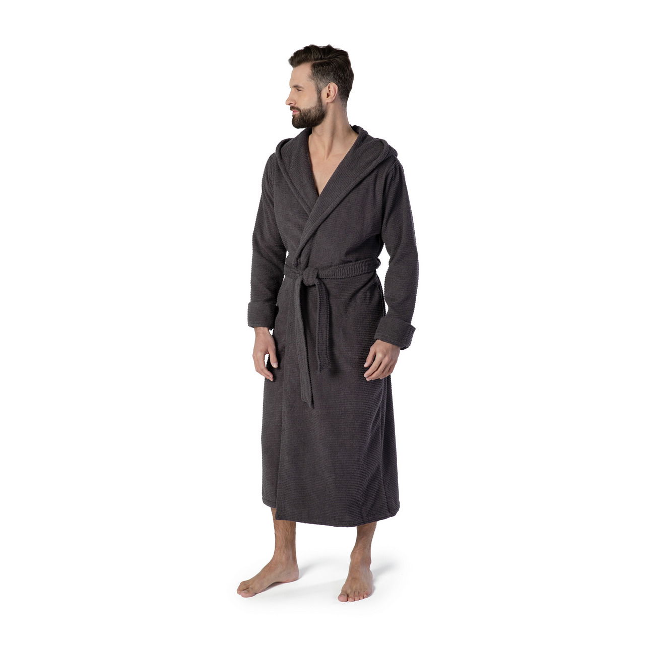 Mann in einem dunkelgrauen Kapuzenbademantel, Größe M, steht barfuß und blickt zur Seite. Frontalansicht.
