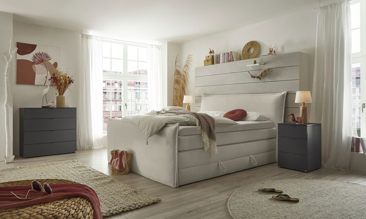 Modernes Boxspringbett in einem hellen Schlafzimmer mit großen Fenstern, seitliche Perspektive