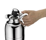 Nahaufnahme einer glänzenden Isolierkanne Juwel aus Edelstahl, die von einer Hand am Griff gehalten wird, während der Deckel geöffnet wird.