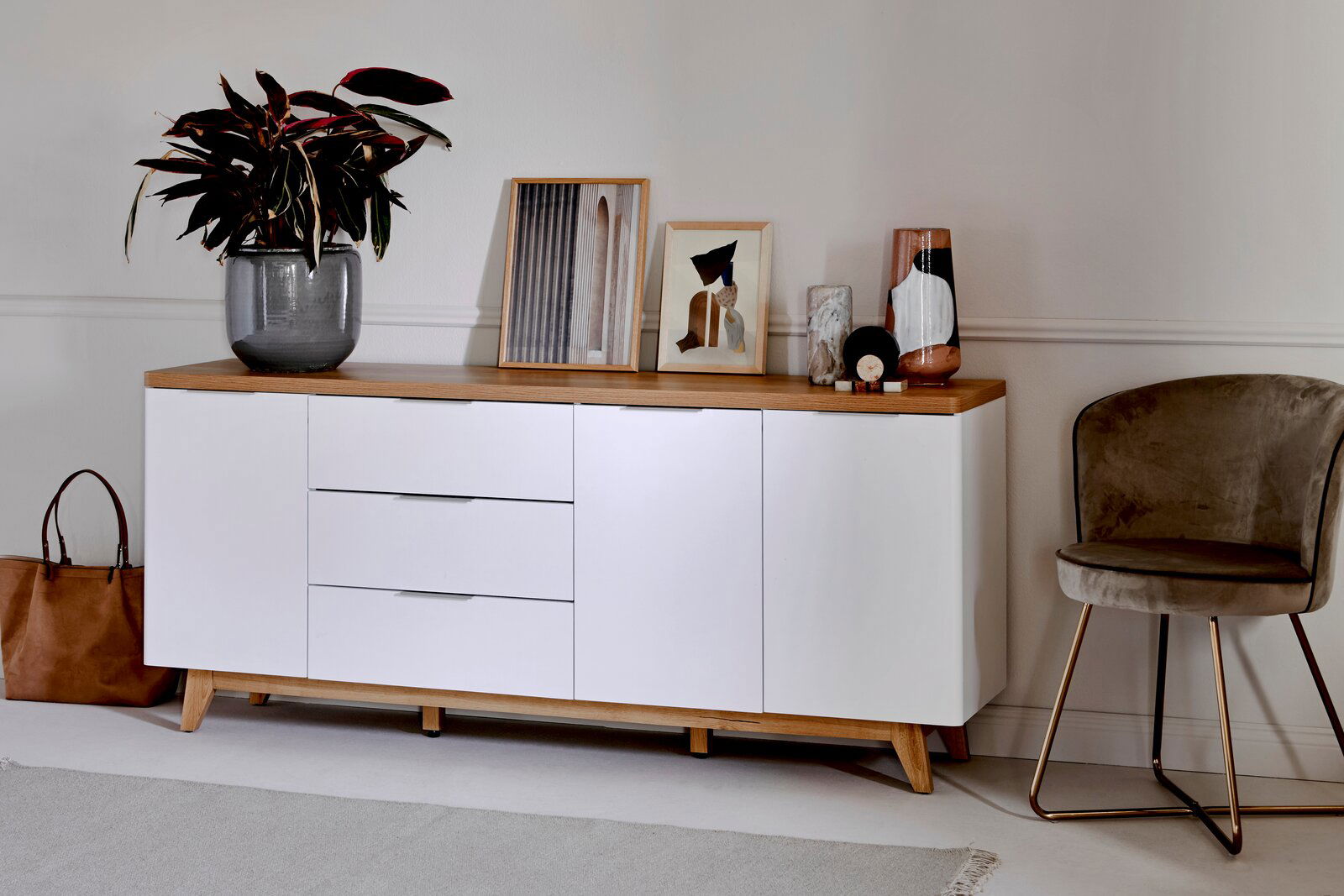 Modernes Sideboard mit weißer Front und Holzoberfläche, dekoriert mit Pflanzen und Kunstwerken, seitliche Perspektive