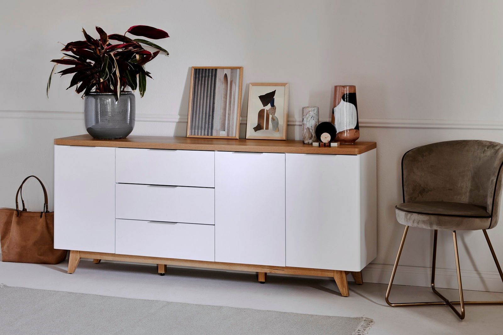 Modernes Sideboard mit weißer Front und Holzoberfläche, dekoriert mit Pflanzen und Kunstwerken, seitliche Perspektive