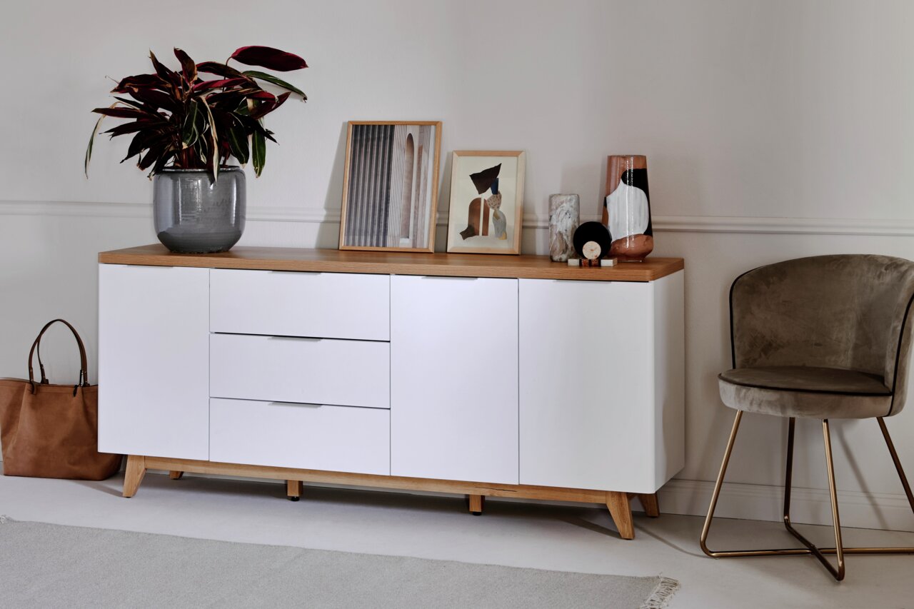 Modern dressoir met witte voorkant en houten oppervlak, versierd met planten en kunstwerken, zijaanzicht