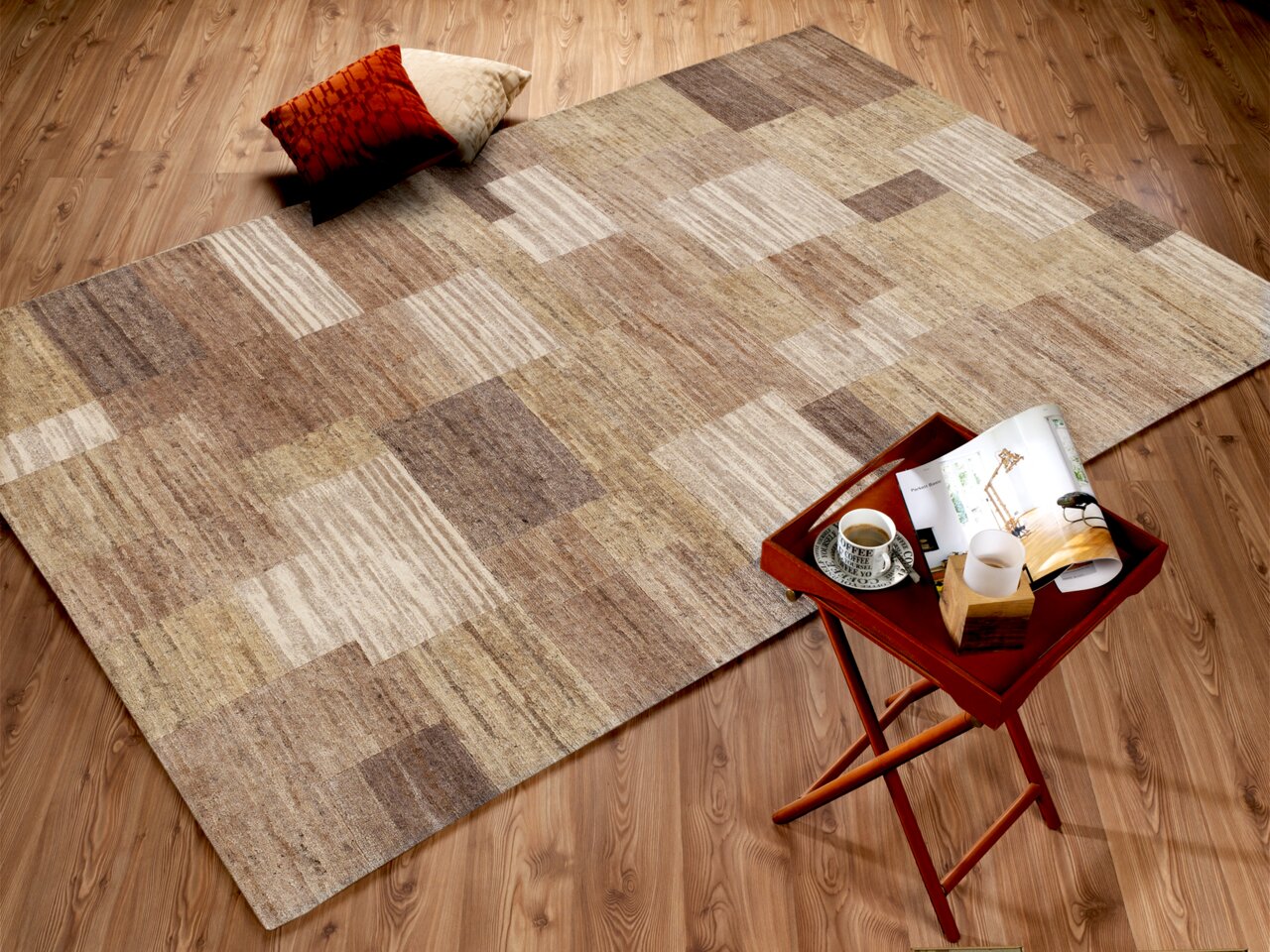 Wollteppich in neutralen Tönen mit geometrischem Muster, von oben fotografiert, auf einem Holzboden mit einem kleinen Tisch und Kissen daneben.