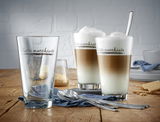 Latte Macchiato-Set mit zwei gefüllten Gläsern und einem leeren Glas, von vorne fotografiert, auf einem Holztisch mit Löffeln und Keksen.