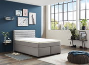 Modernes Boxspringbett in einem stilvoll eingerichteten Raum mit blauer Akzentwand und großen Fenstern, seitliche Perspektive.