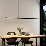 Moderne, slanke zwarte led-hanglamp in de vorm van een lange lichtbalk boven een houten tafel met twee stoelen, een vaas en serviesgoed, frontaal gefotografeerd vanuit een iets hoger perspectief