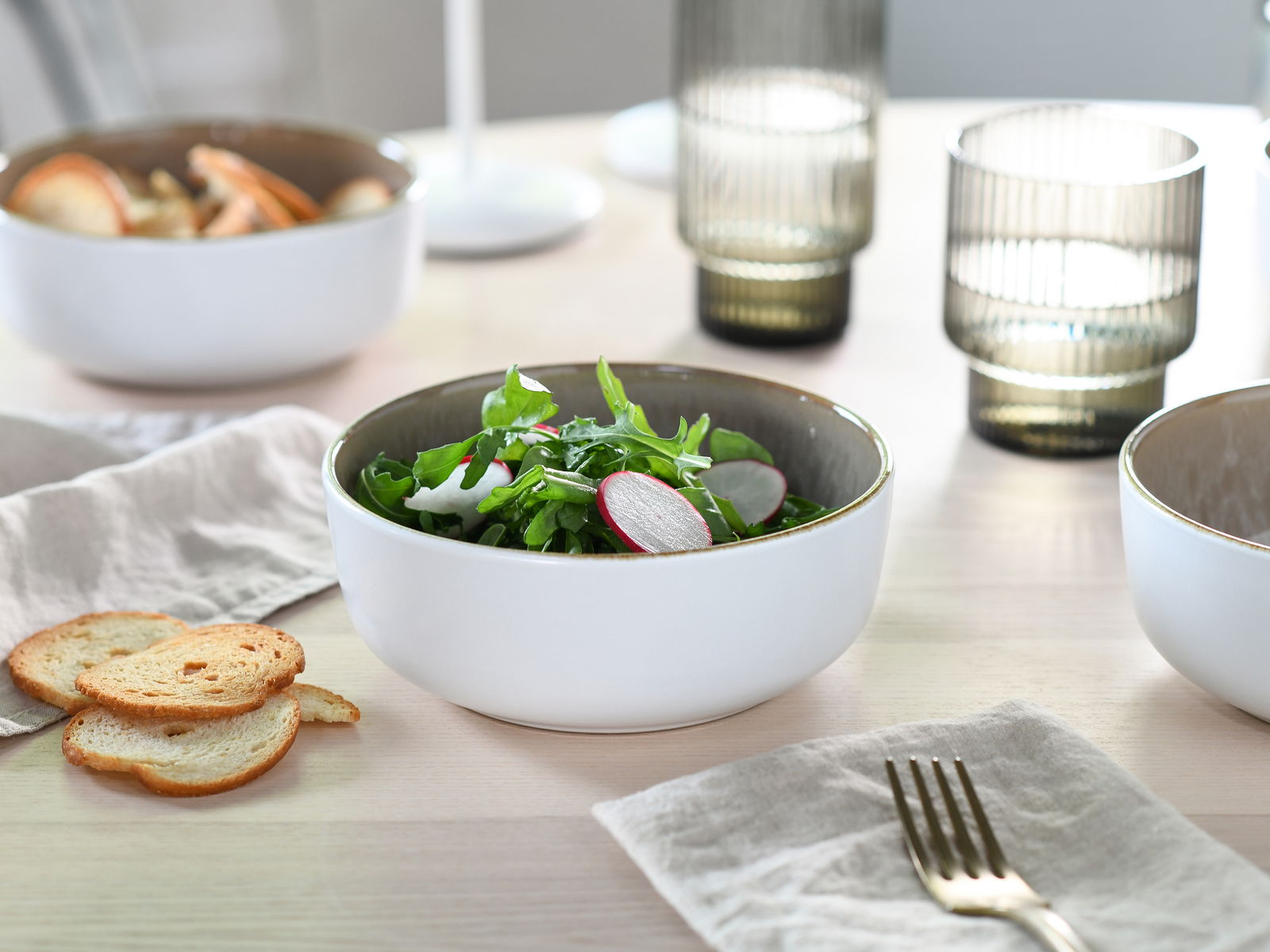 Elegantes Kombiservice in Sandfarbe, bestehend aus Schalen und Gläsern, auf einem gedeckten Tisch von oben fotografiert.