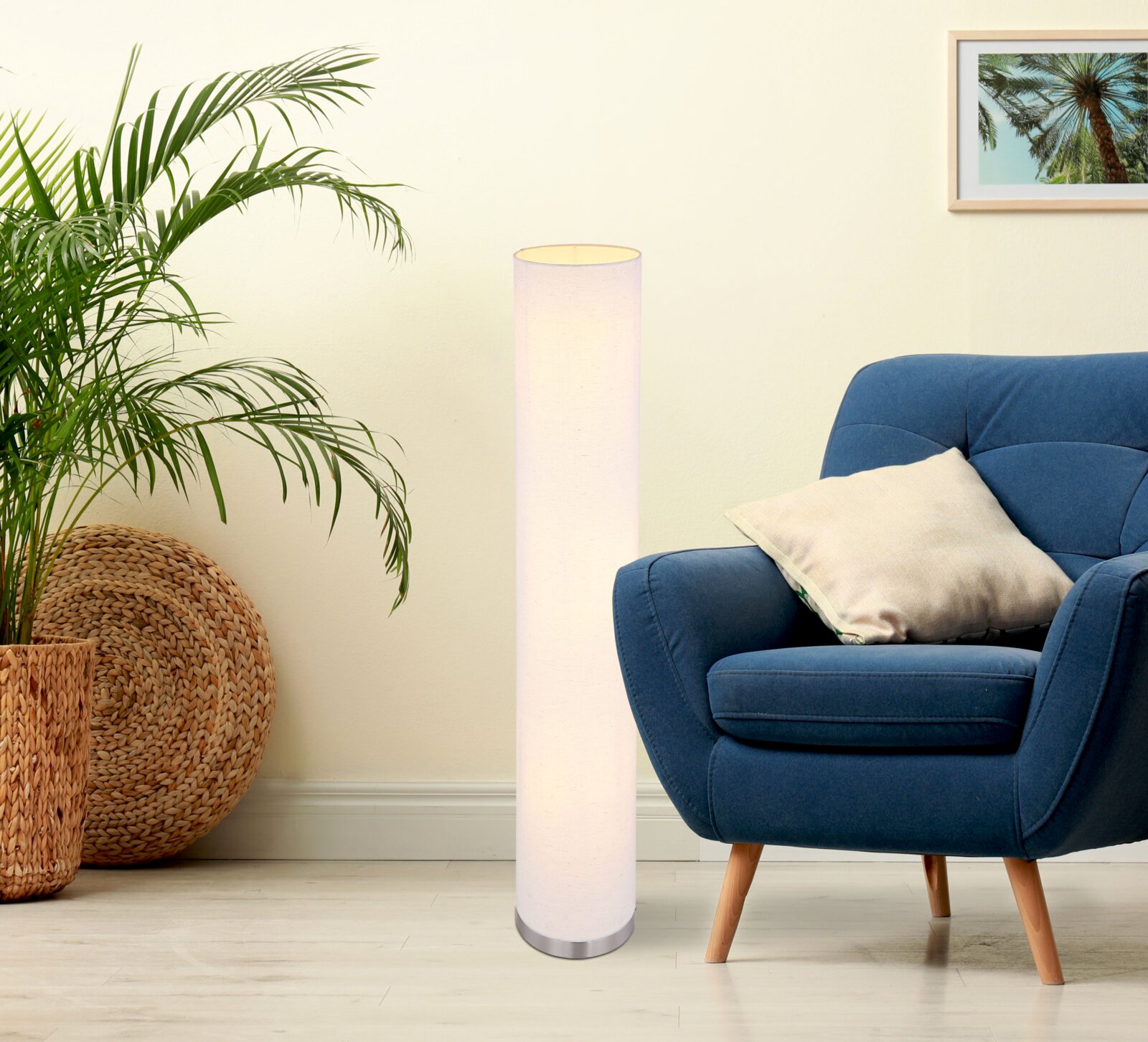 Schlanke, zylindrische Stehlampe mit weißem Stoffschirm und Metallfuß neben blauem Sessel in modernem Wohnzimmer, frontale Perspektive.