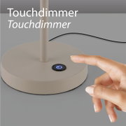 Nahaufnahme aus leicht schräger Seitenansicht: runder Lampenfuß in Beige mit leuchtendem Touchdimmer-Powerknopf, daneben ein Finger zum Berühren.