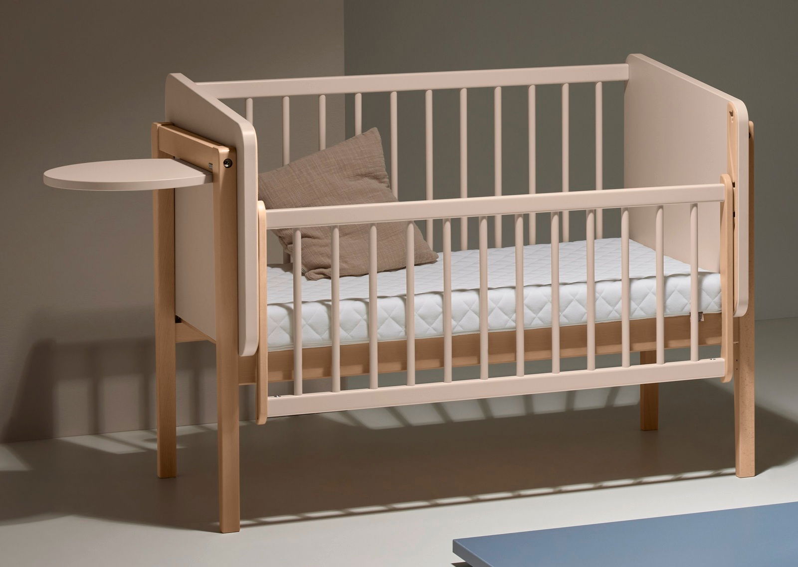 Kinderbett mit hellem Holzrahmen und abgerundeten Ecken, seitlich angebrachtem kleinen Tischchen, von schräg vorne fotografiert.