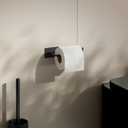 Moderner Toilettenpapierhalter aus Edelstahl in seitlicher Perspektive, montiert an einer beigen Wand mit einer Rolle Toilettenpapier.