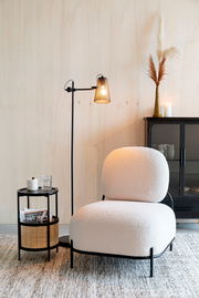 Beistelltisch MAKATO aus schwarzem Metall mit zwei Ebenen, eine mit Rattan-Elementen, im modernen Wohnzimmer neben einem Sessel, aus seitlicher Perspektive.