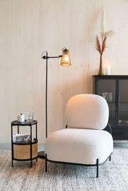 Beistelltisch MAKATO aus schwarzem Metall mit zwei Ebenen, eine mit Rattan-Elementen, im modernen Wohnzimmer neben einem Sessel, aus seitlicher Perspektive.