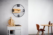 Moderne Wanduhr mit schwarzem Metallrahmen und Holzelementen, frontal an einer weißen Wand montiert.