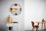 Moderne Wanduhr mit schwarzem Metallrahmen und Holzelementen, frontal an einer weißen Wand montiert.