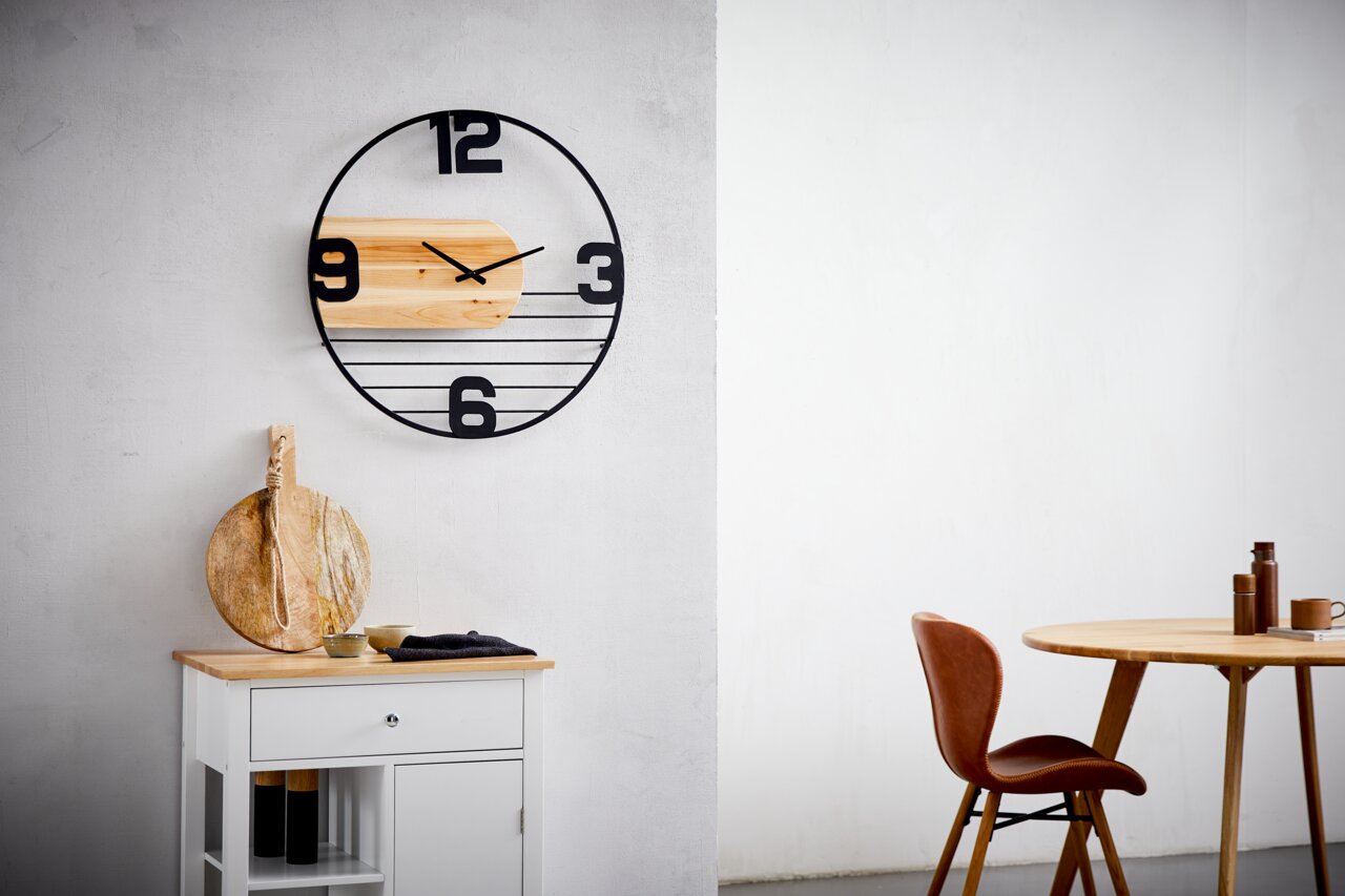 Moderne Wanduhr mit schwarzem Metallrahmen und Holzelementen, frontal an einer weißen Wand montiert.