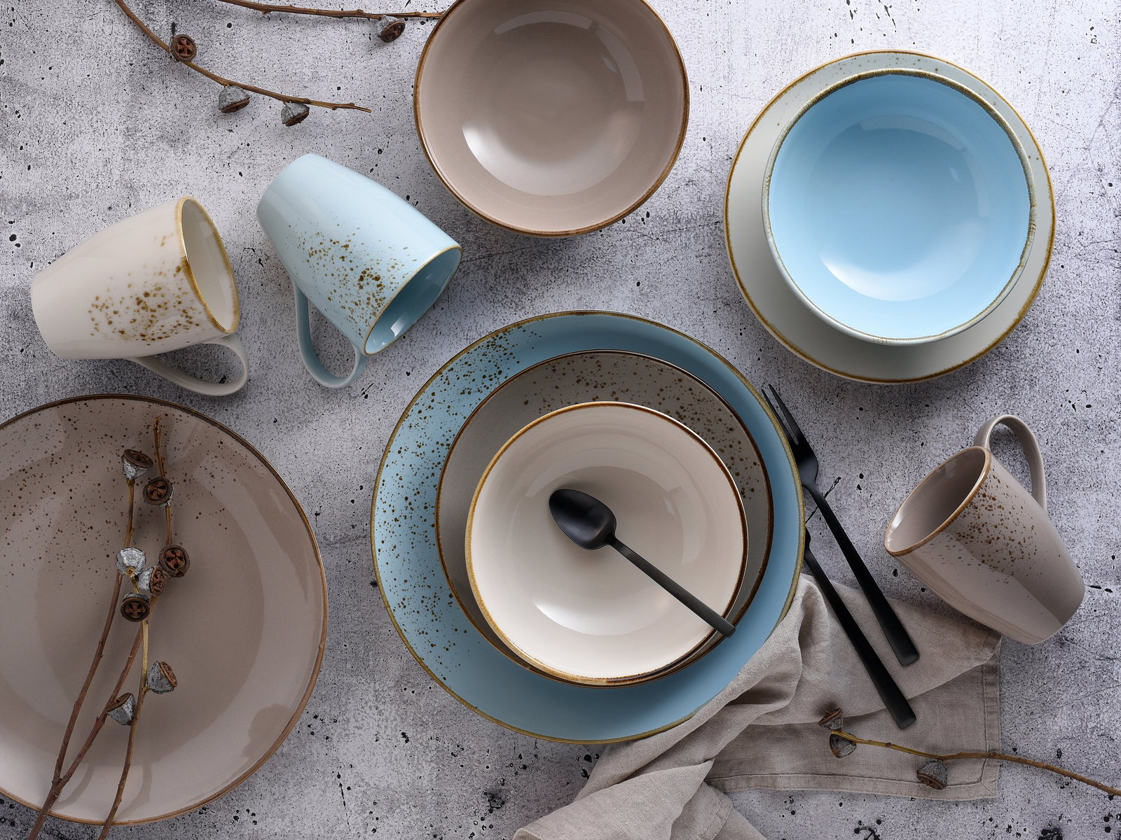 Vogelperspektive auf ein stilvolles 16-teiliges Kombiservice-Set mit Tellern, Schalen und Tassen in sanften Beige- und Blautönen, dekoriert mit Zweigen und Besteck.