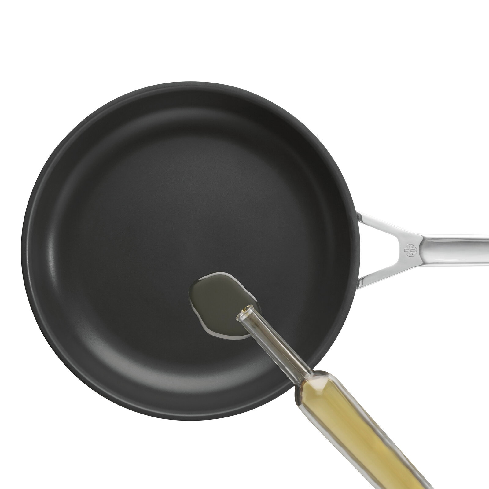 Schwarze Bratpfanne mit Edelstahlgriff, in die aus einer Glasflasche Öl gegossen wird, Draufsicht von oben auf weißem Hintergrund