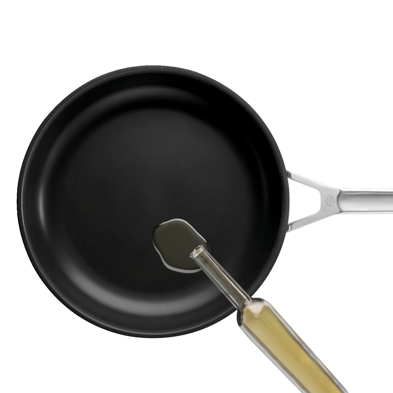 Schwarze Bratpfanne mit Edelstahlgriff, in die aus einer Glasflasche Öl gegossen wird, Draufsicht von oben auf weißem Hintergrund