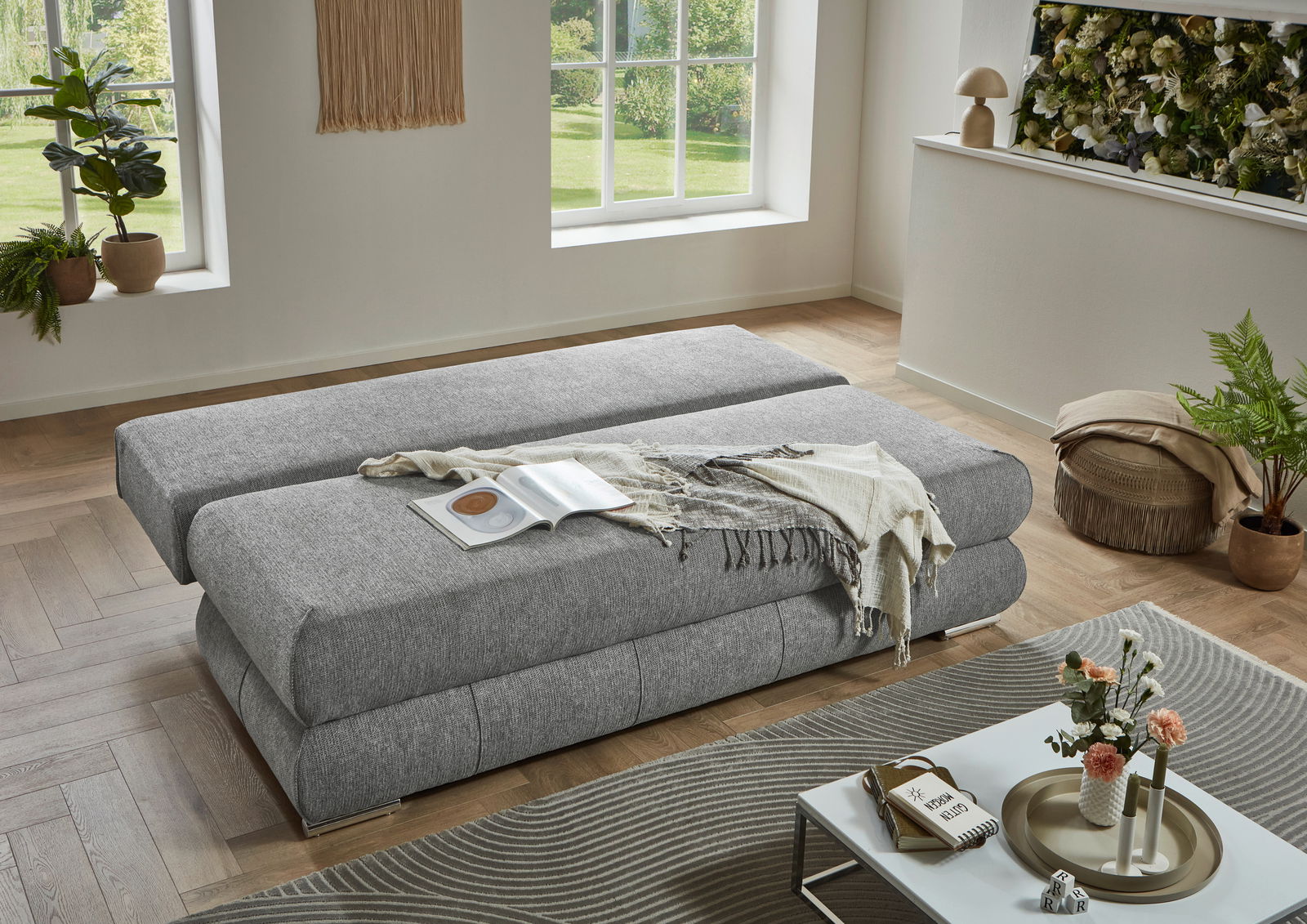 Graues Funktionssofa in einem modernen Wohnzimmer, von oben betrachtet, mit einem Buch und einer Decke darauf.
